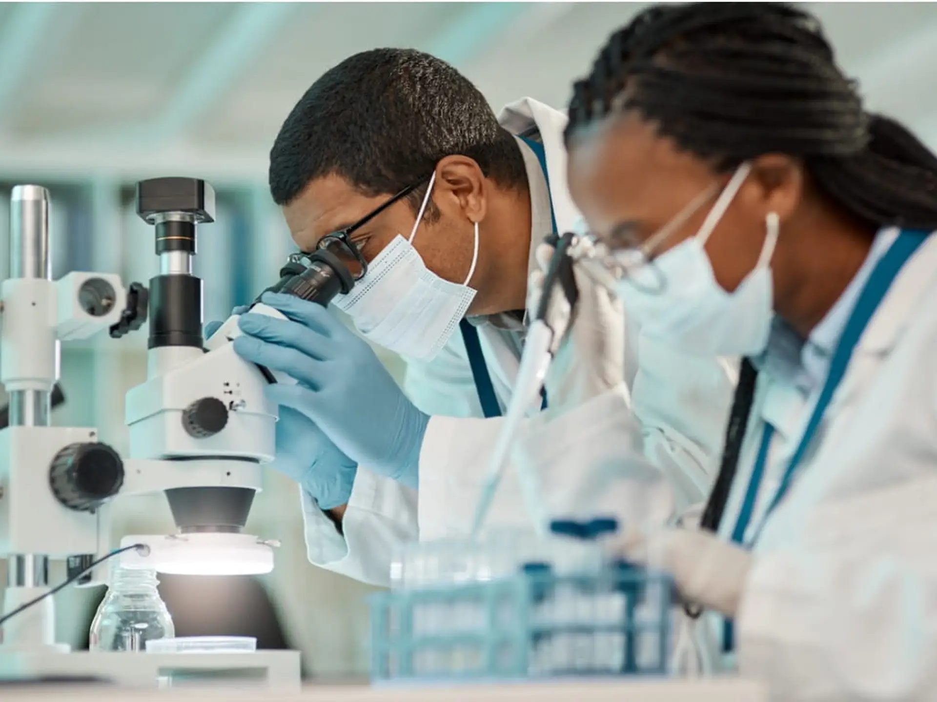 scientists wearing mask in lab looking intro microscope