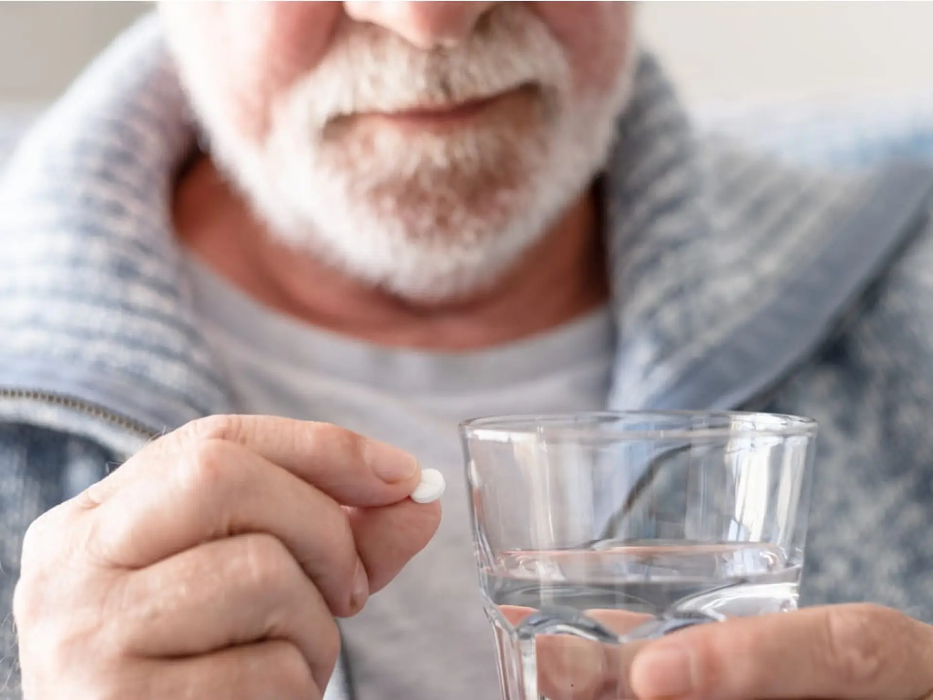 man taking a white pill with a glass of water