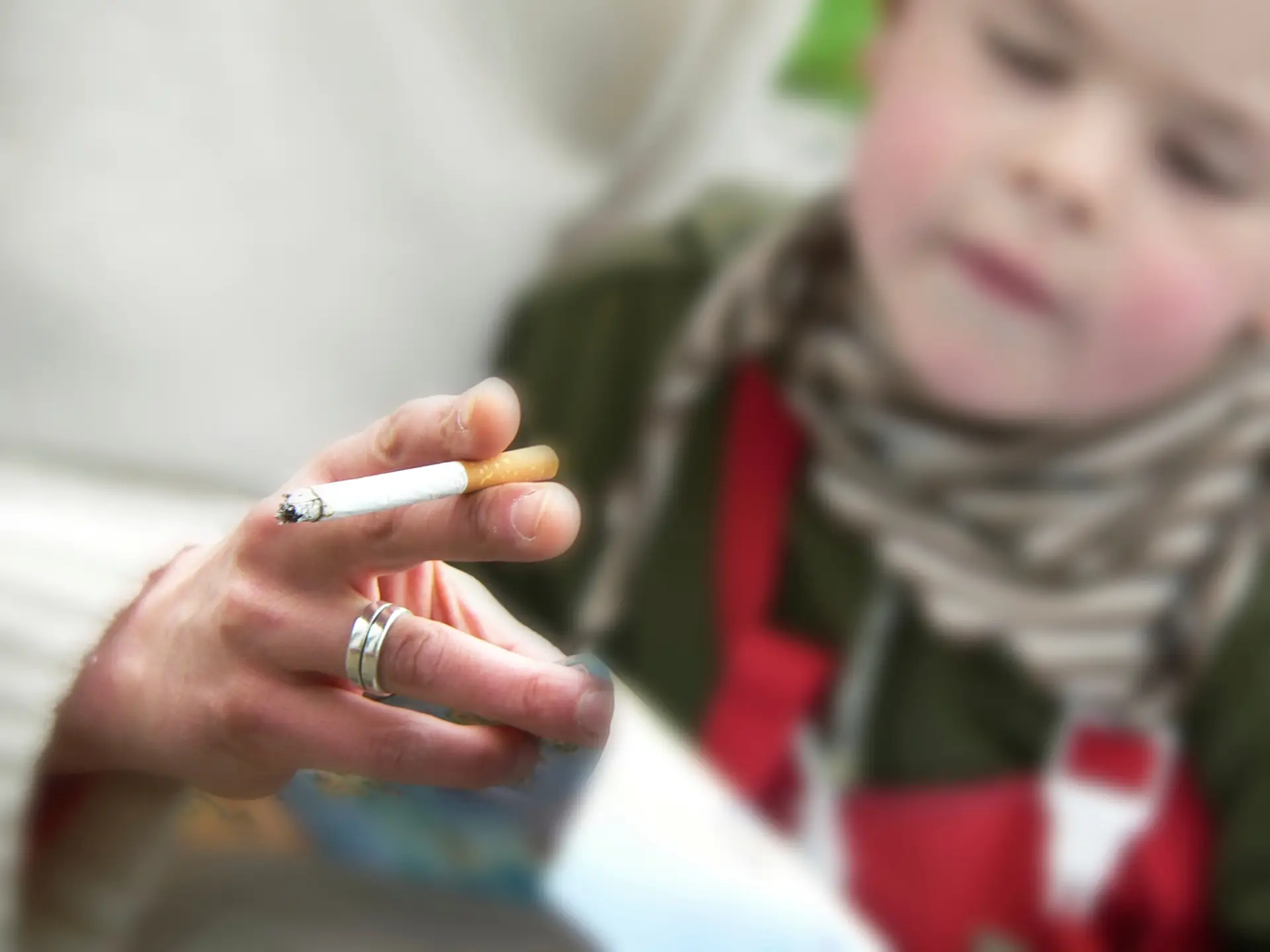 adult holding a cigarette in front of a child