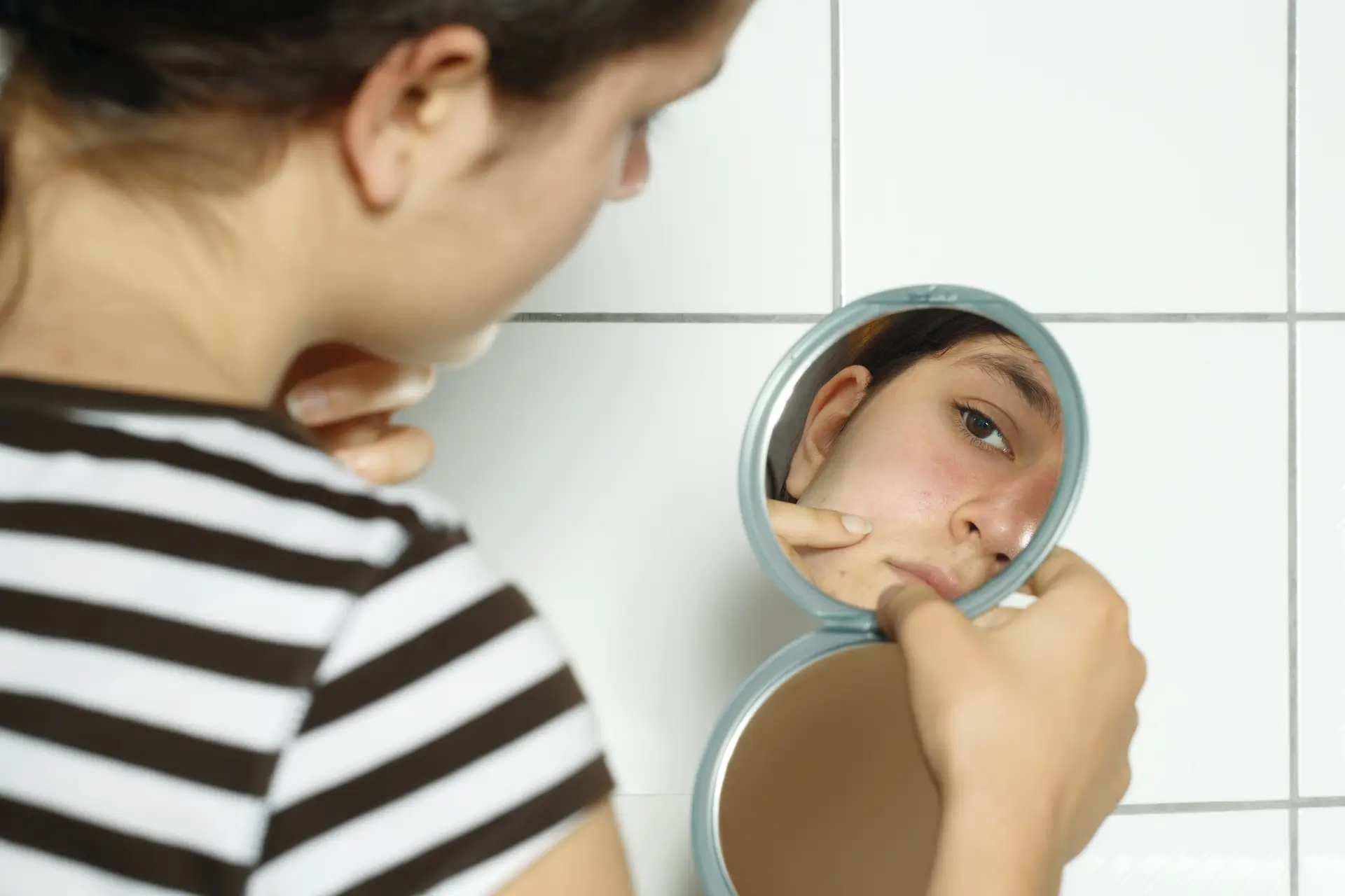 Woman checking pimple in hand mirror