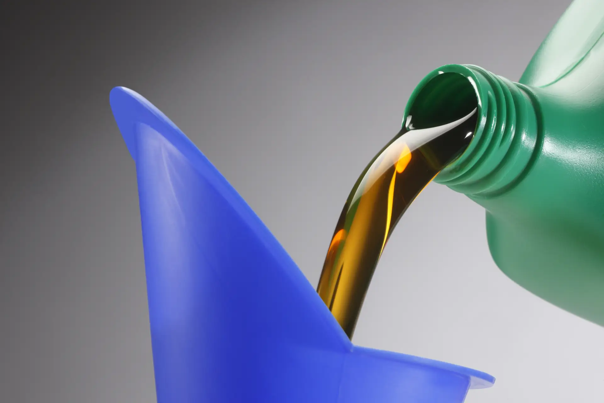 Green bottle pouring motor oil into a blue funnel