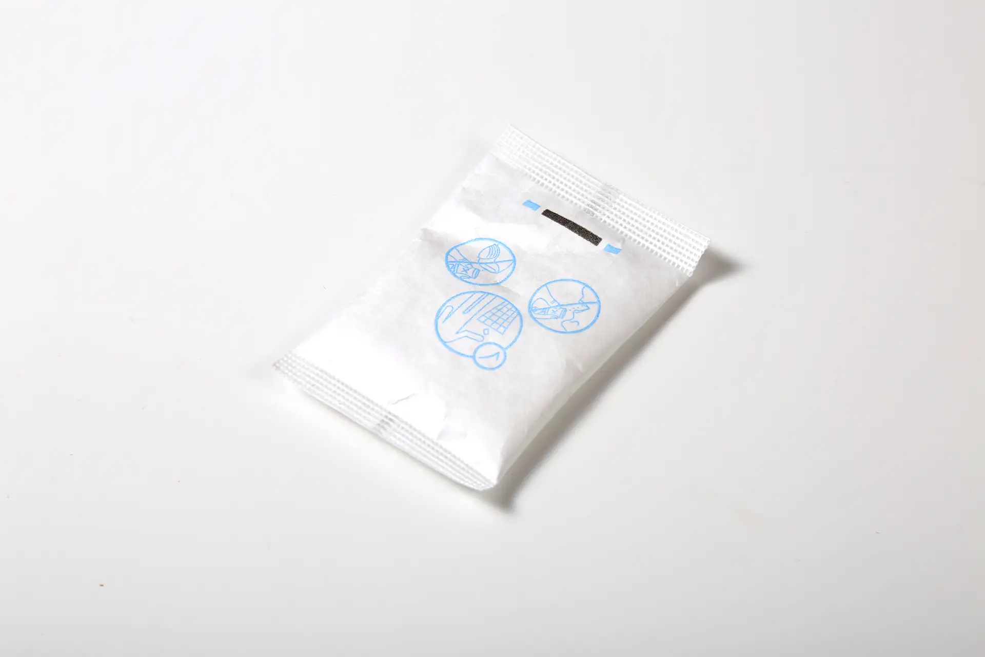 A small, sealed white packet with blue icon illustrations on the front, lying on a plain white surface.