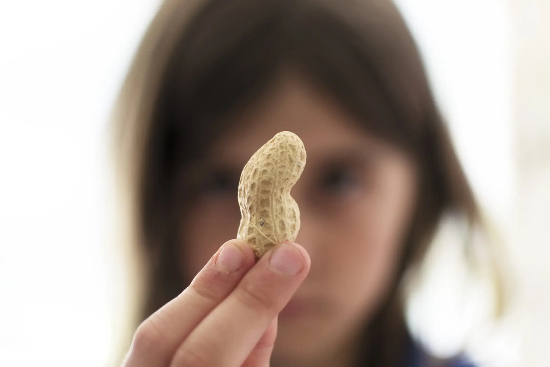 Child holding a peanut in focus, with face blurred in the background.