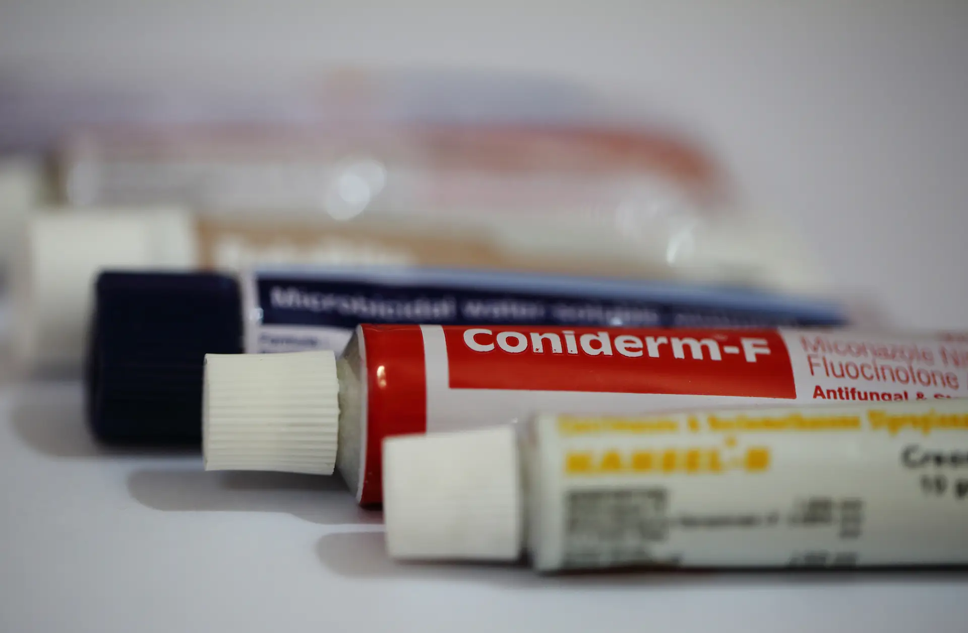 Close-up of several tubes of topical creams, partially focused, with one labeled "Coniderm-F" in the foreground.