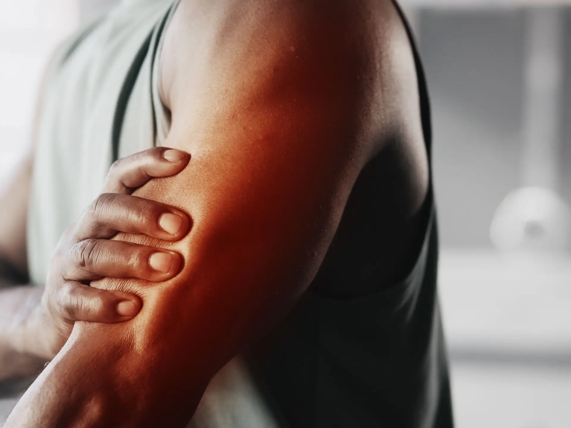 Person holding their upper arm, indicating discomfort or muscle pain, with a background of soft focus indoors.