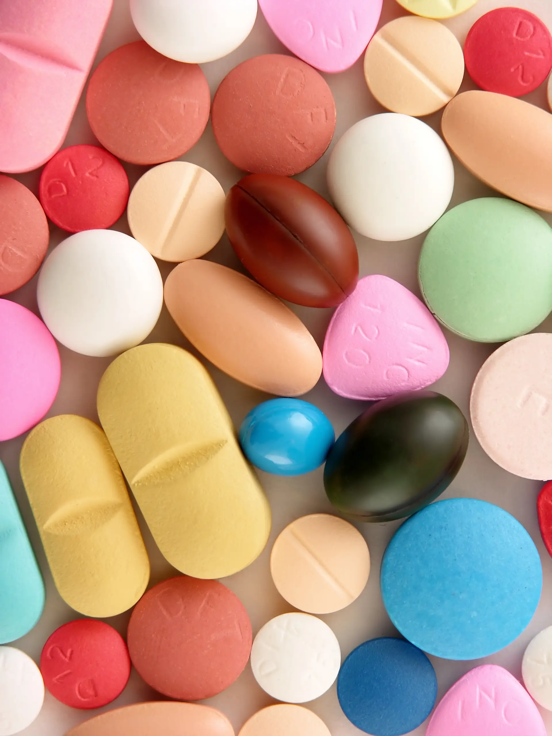 A variety of colorful pills and tablets in different shapes and sizes scattered on a plain surface.