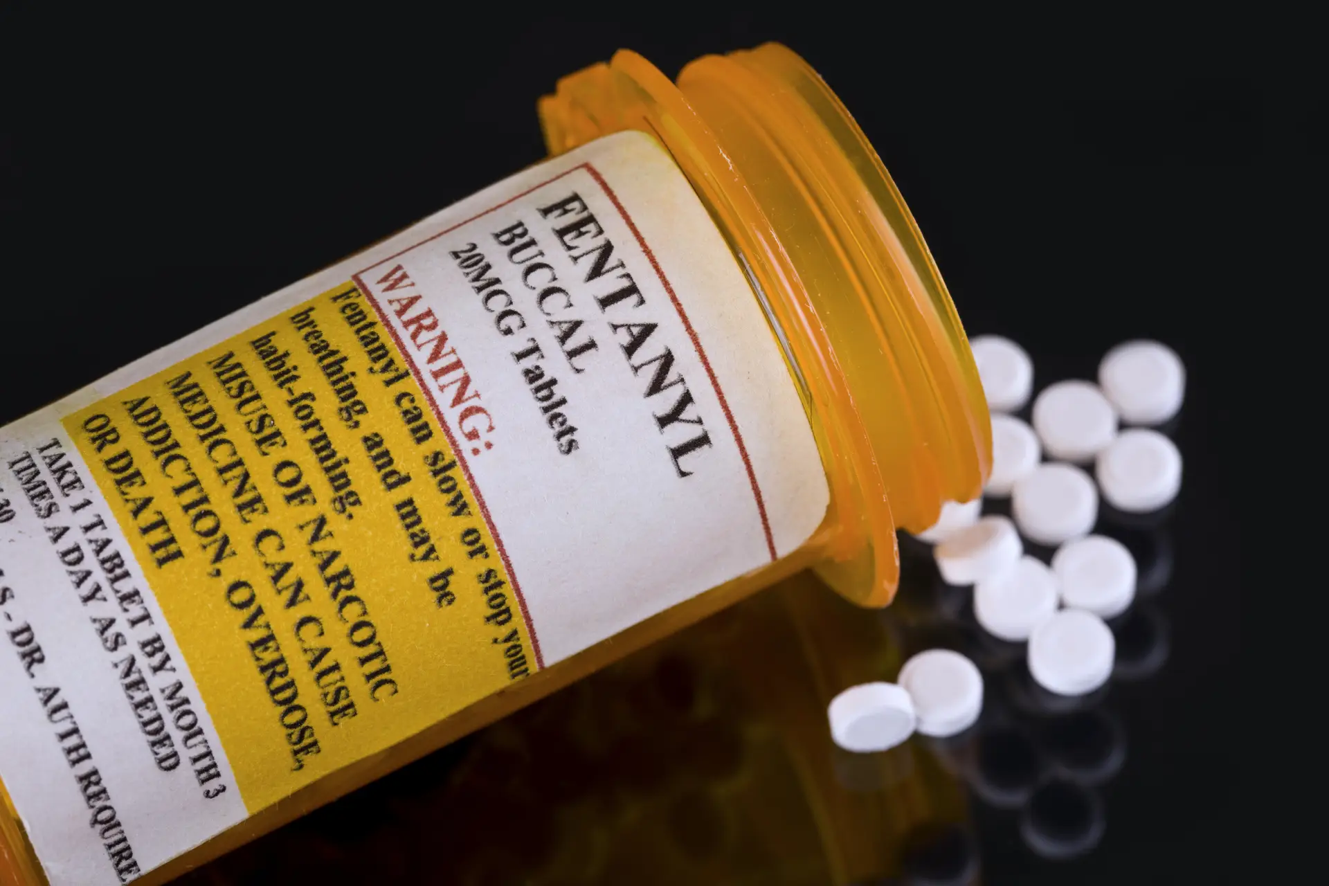 A prescription bottle labeled "Fentanyl Buccal 20 MCG Tablets" spills white pills; warning labels highlight overdose and addiction risks.