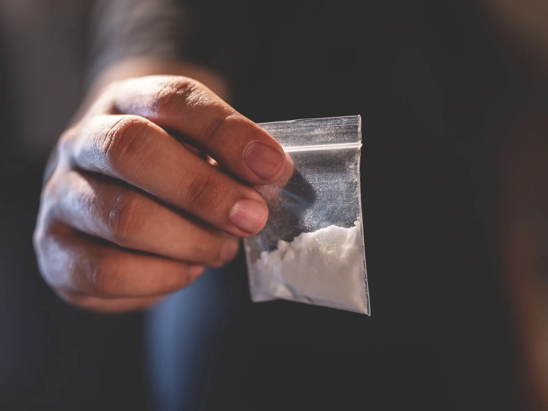 Hand holding a small plastic bag containing white powder against a blurred background.