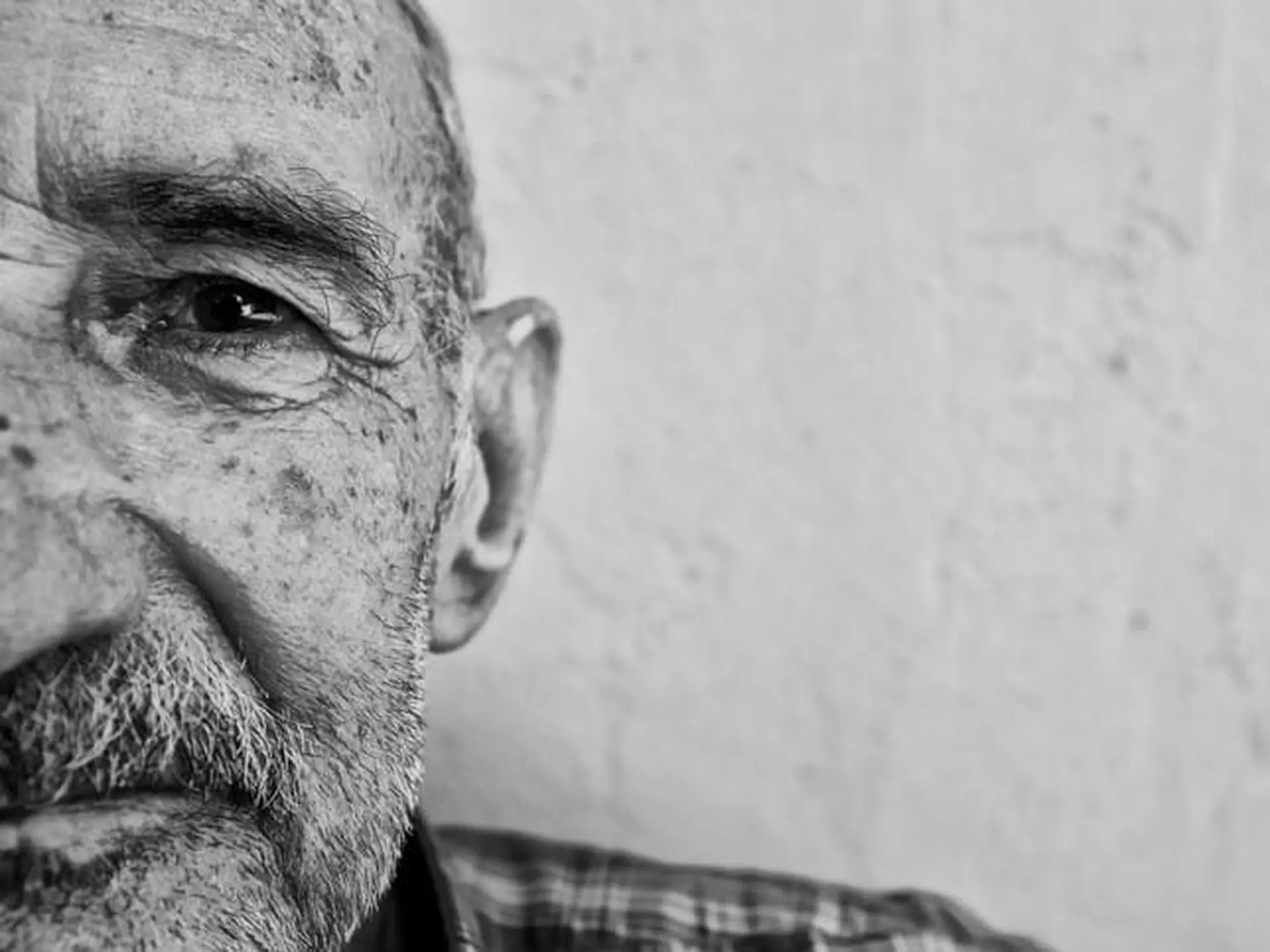 Close-up black and white image of an elderly man's face, focusing on his eye and textured skin, with a neutral background.